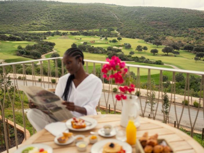 A woman reads a newspaper on a Viceroy Ombria Algarve patio and the green Algarve hills behind her